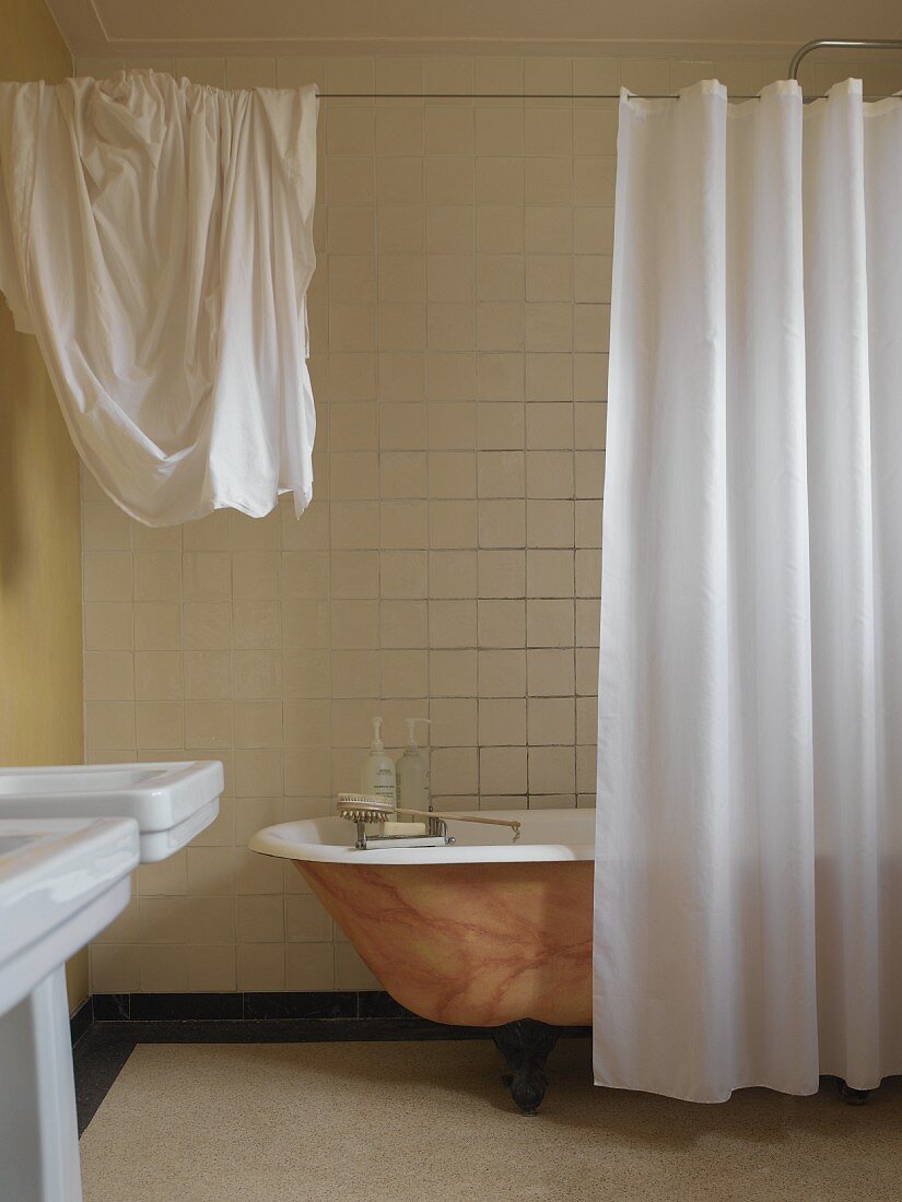 Freistehende Wanne mit marmorierter Farbgebung hinter weißem Vorhang in einfachem Bad