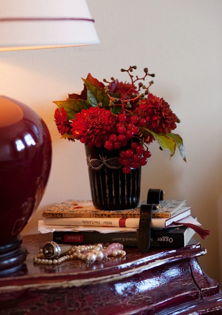 Autumnal bouquet, books, bead necklace and lamp on Baroque-style bedside table