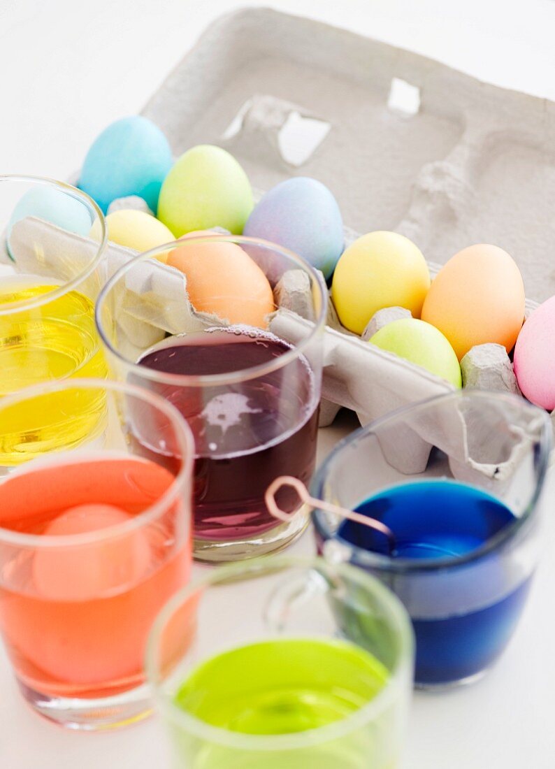 Becher mit Eierfarben und gefärbte Ostereier im Eierkarton
