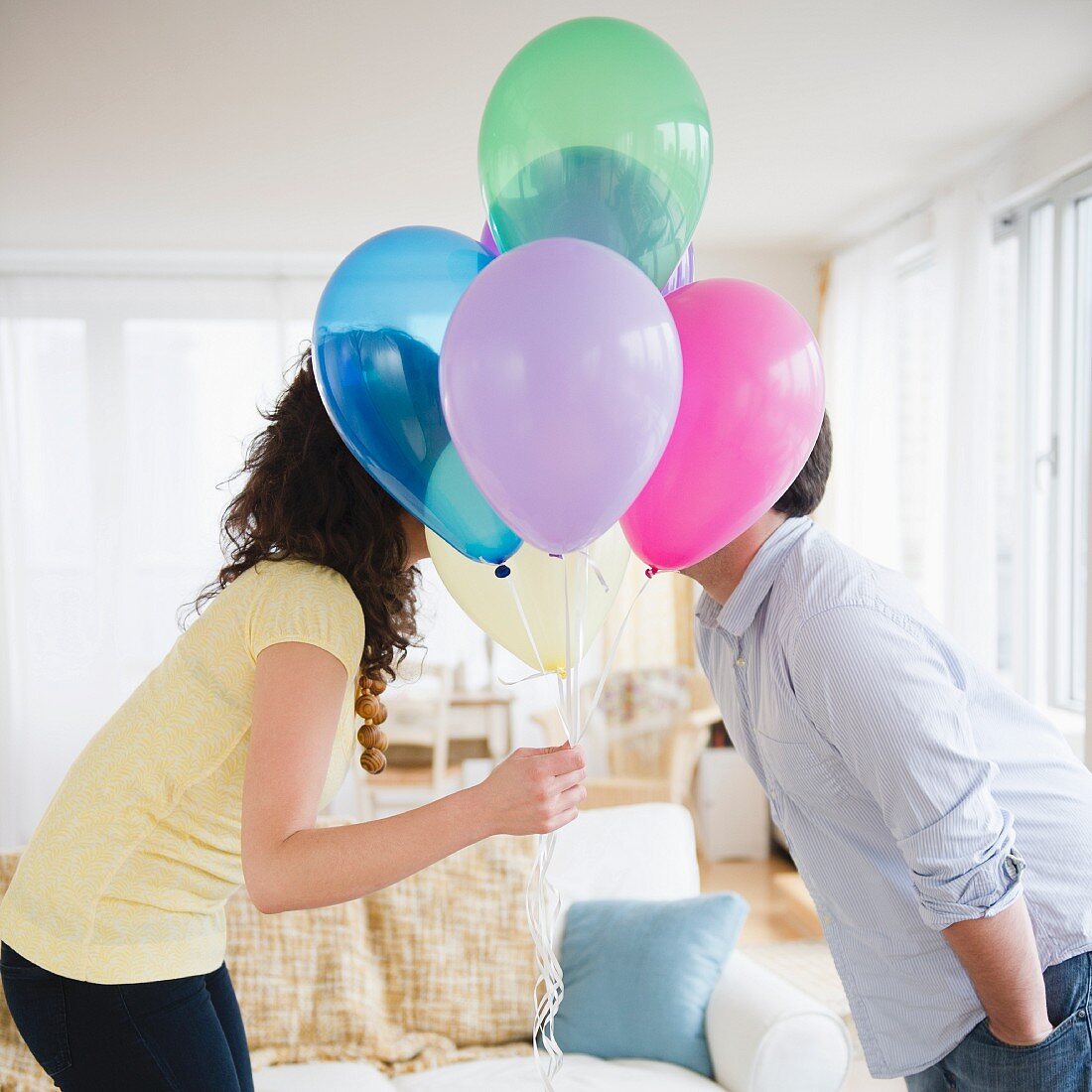 Couple kissing behind bunch of colorful balloons