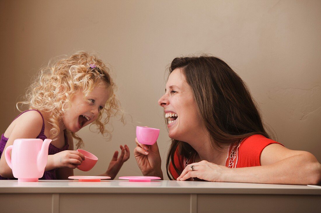 Mother and daughter drinking tea from doll's tea set