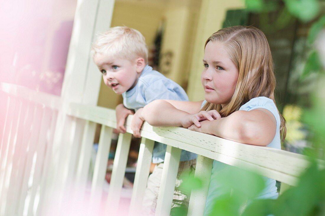 Bruder und Schwester blicken über das Geländer einer Veranda