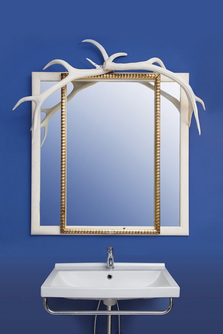 Spiegel mit weißem und goldenen Rahmen und Geweihdekoration über Waschbecken