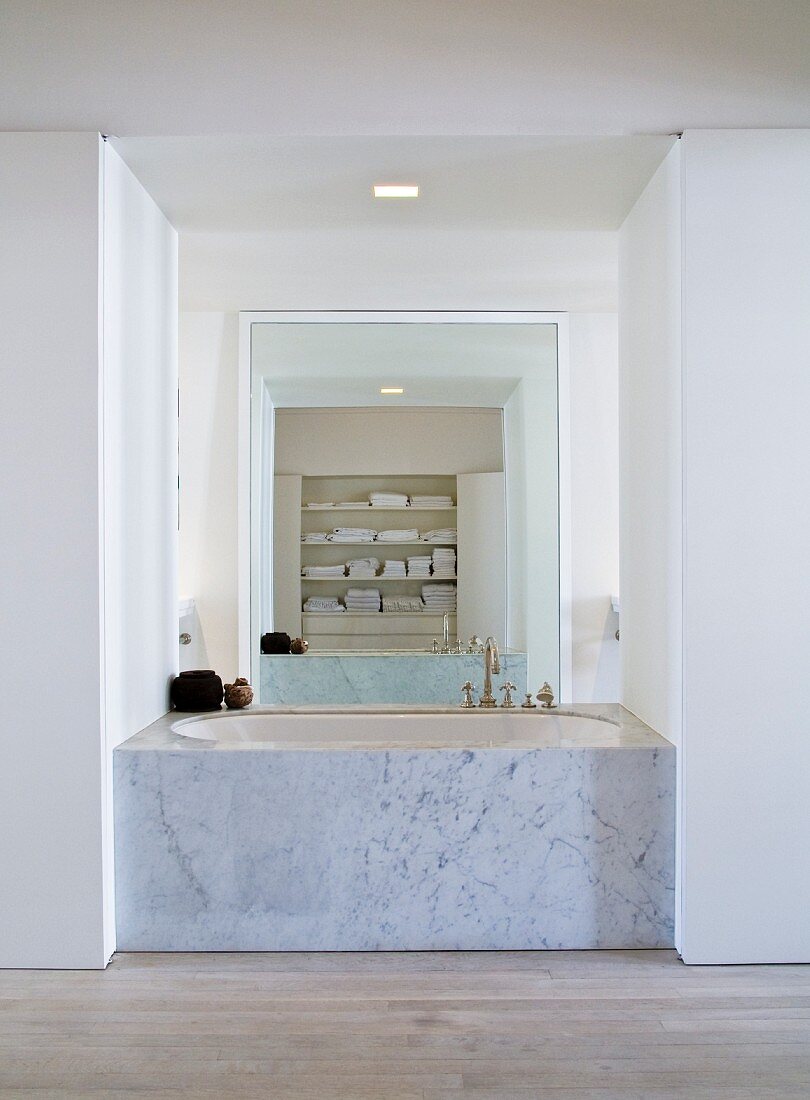 Badewanne mit Marmor Seitenwand in offene Nische eingebaut und raumhoher Spiegel gegenüber an Wand
