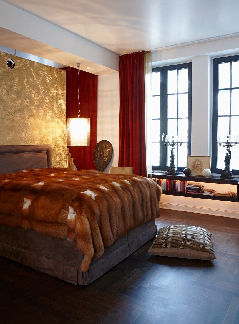 Grand bedroom with fur blanket on impressive double bed; shiny, gold wall behind upholstered headboard