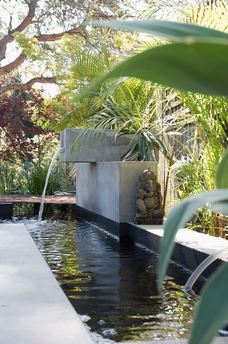 Ganesh sculpture on the edges of a rectangular water feature surrounded by palms