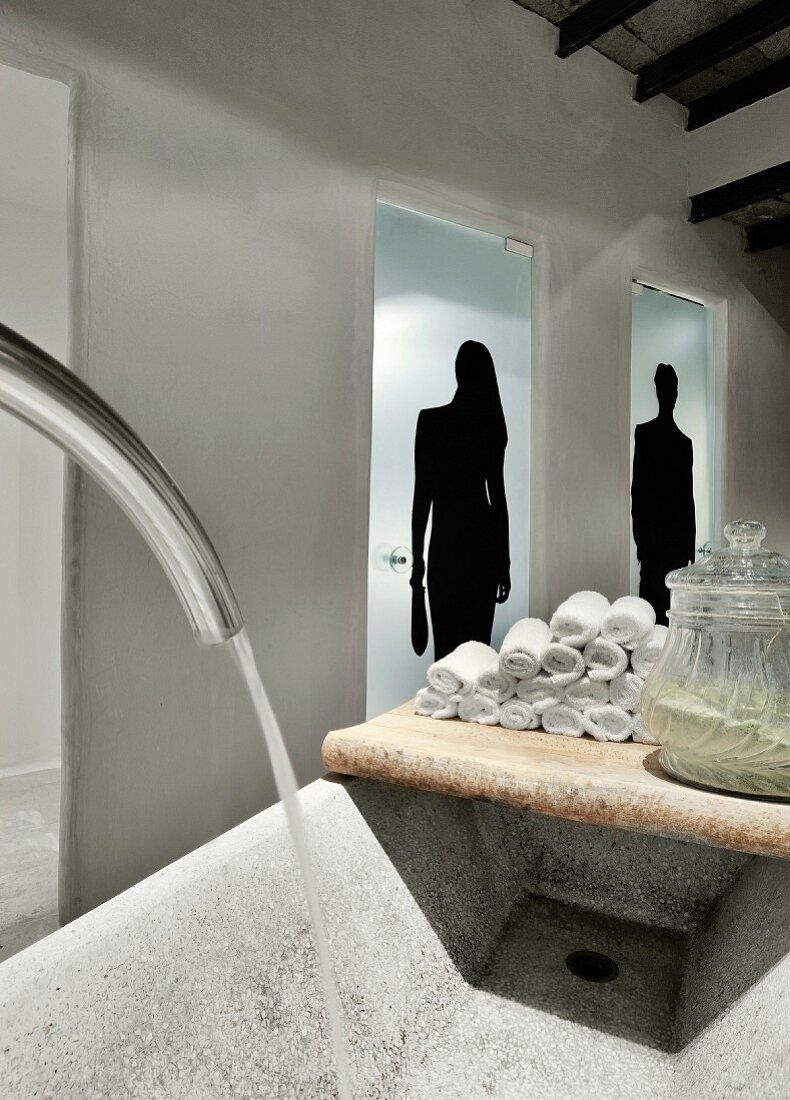 Towels on vintage wooden board next to rustic stone trough in front of glass doors with silhouette motifs of a man and a woman