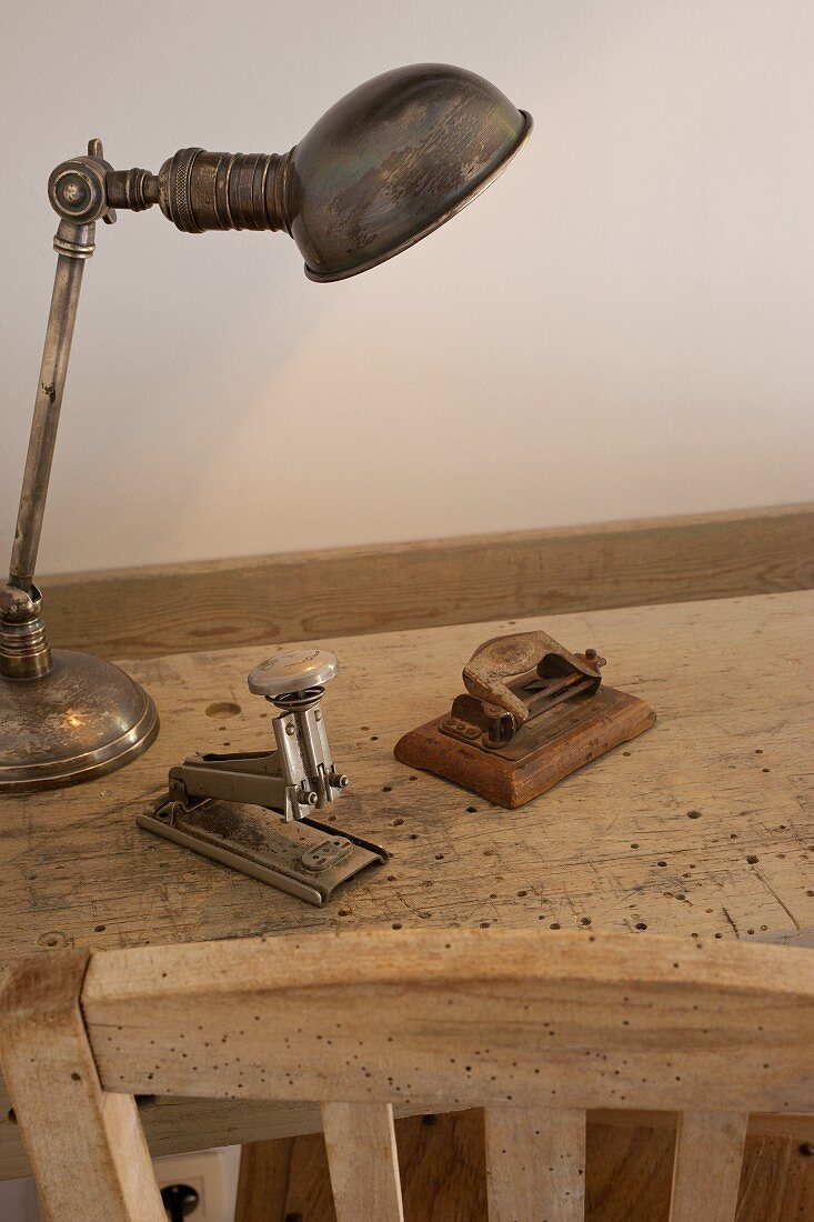 Silberne Schreibtischlampe, Locher und Hefter auf wurmstichigem Holztisch
