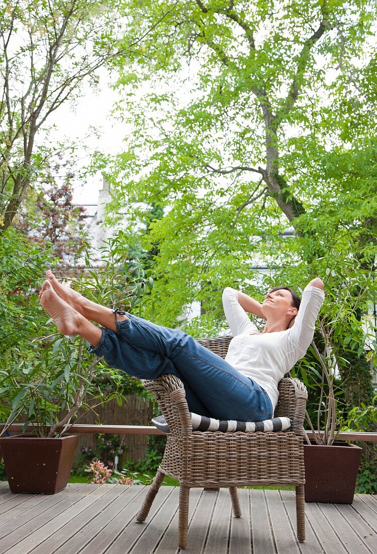 Frau mit ausgestreckten Beinen auf einem Gartenstuhl auf der Terrasse