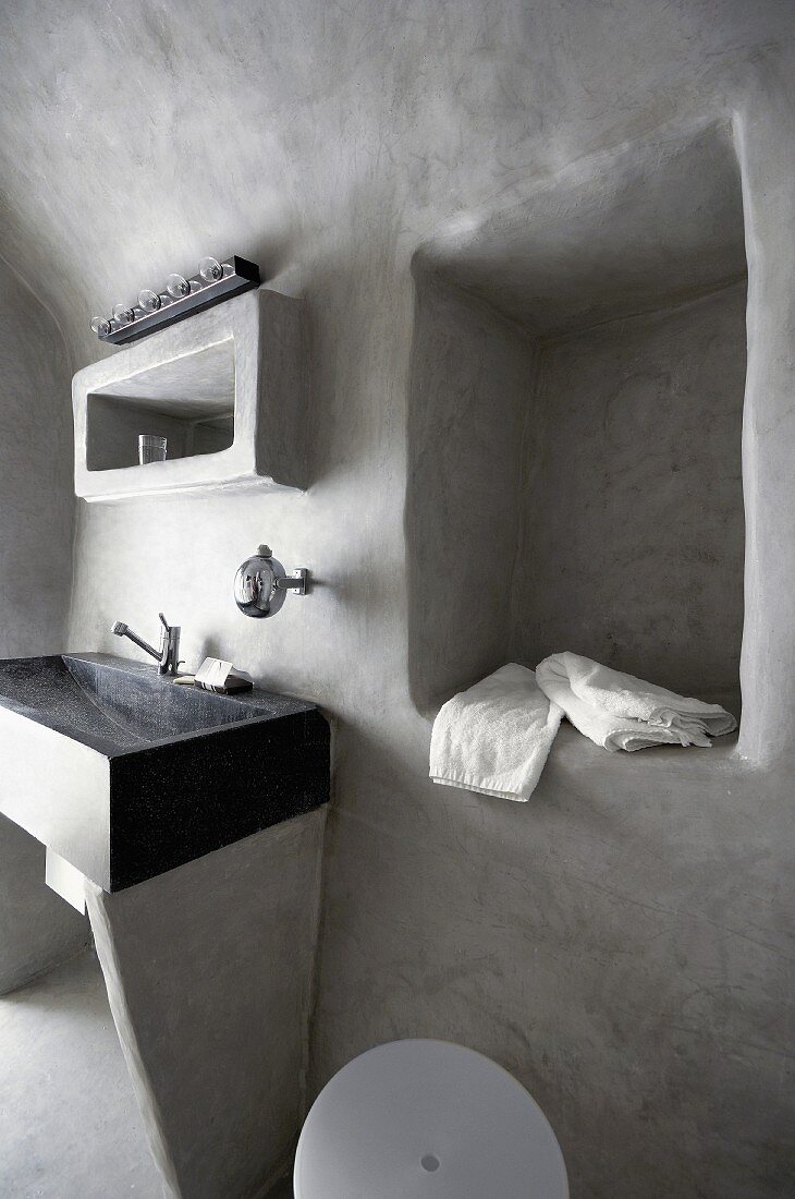 Naturstein-Waschtisch und Nischen in der hellgrau geschlemmten Wand eines minimalistischen Badezimmers