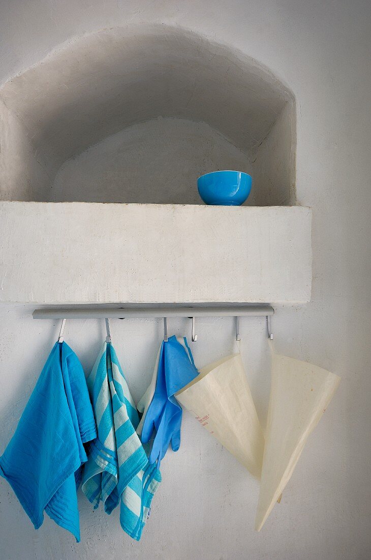 Blaue Schale in geschlemmter Mauernische; Geschirrtücher und Tüten an Haken