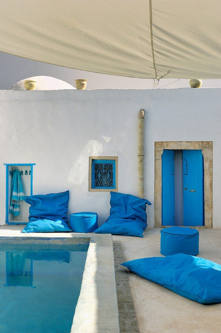 Innenhof im nordafrikanischen Stil mit blauen Sitzsäcken und Polsterhockern um ein Wasserbecken