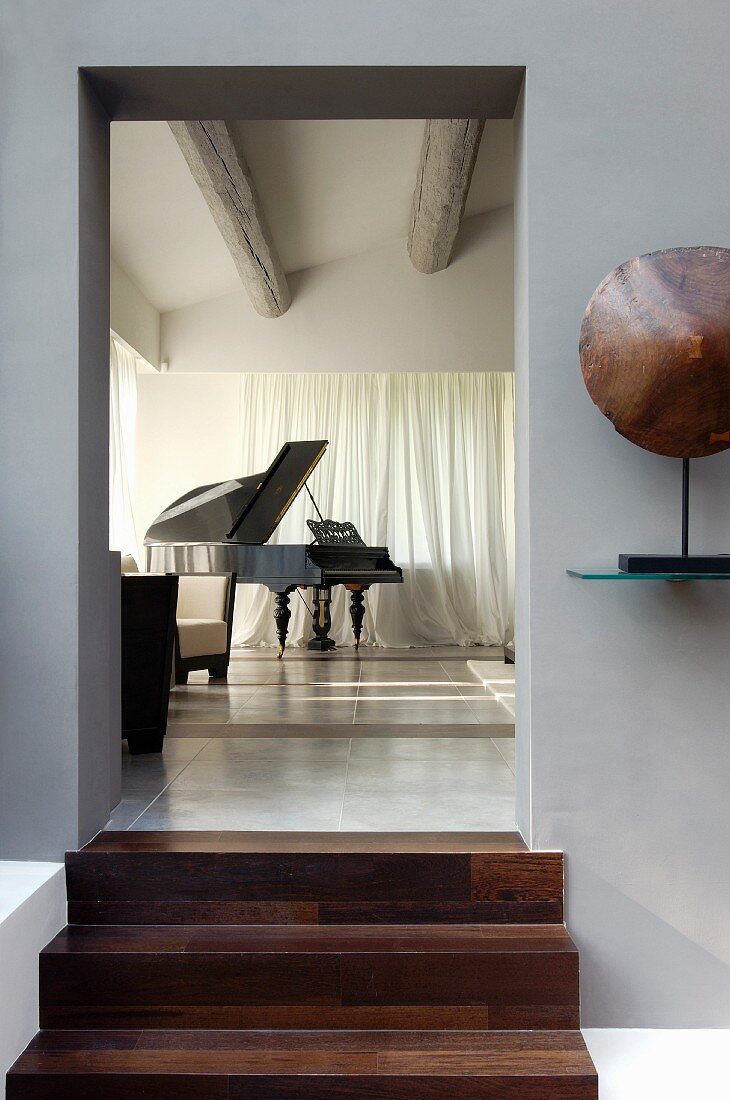 View from grey-painted foyer through open doorway with wooden steps into modernised interior with grand piano
