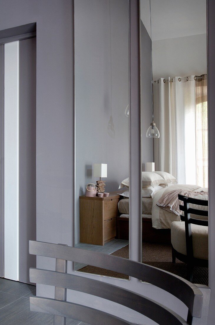 Holz Rückenlehne eines Sessels vor Spiegel mit reflektiertem Schlafzimmer an grauer Wand