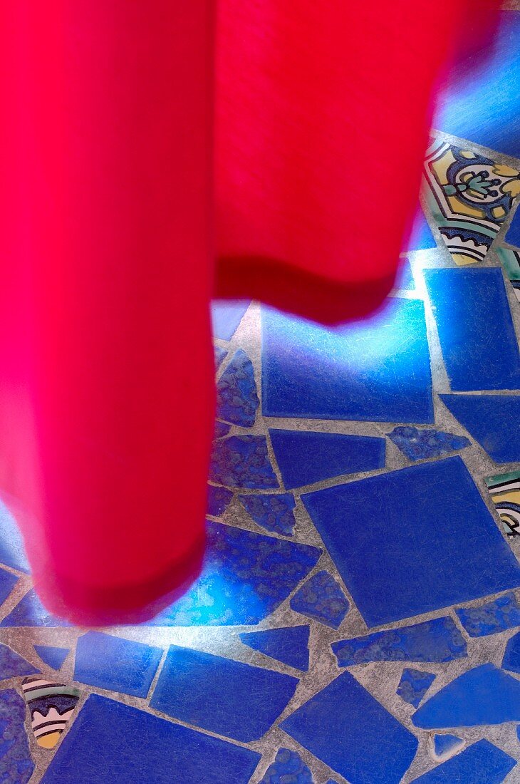 Blaue Fliesenbruchstücke im Mosaikstil auf Boden und beleuchteter langer roter Vorhang