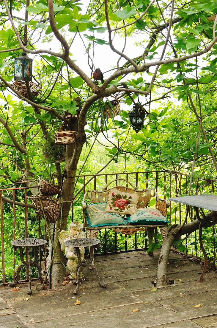 Terrasse mit Metall Blumentischen vor Vintage Gartenbank und am Baum hängende Körbe und Laternen
