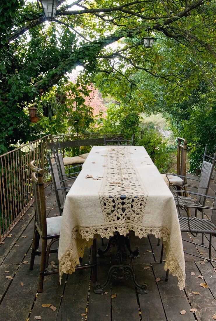 Tischdecke mit Spitzeneinsatz und Metall Stühle auf Holzterrasse in dicht bewachsenem Garten