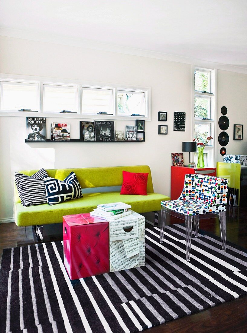 Frühlingsgrüne Couch in modernem Wohnzimmer mit Designerstuhl und originellem Couchtisch aus bedrucktem Pappkarton; Fensterschlitze sorgen für die nötige Helligkeit