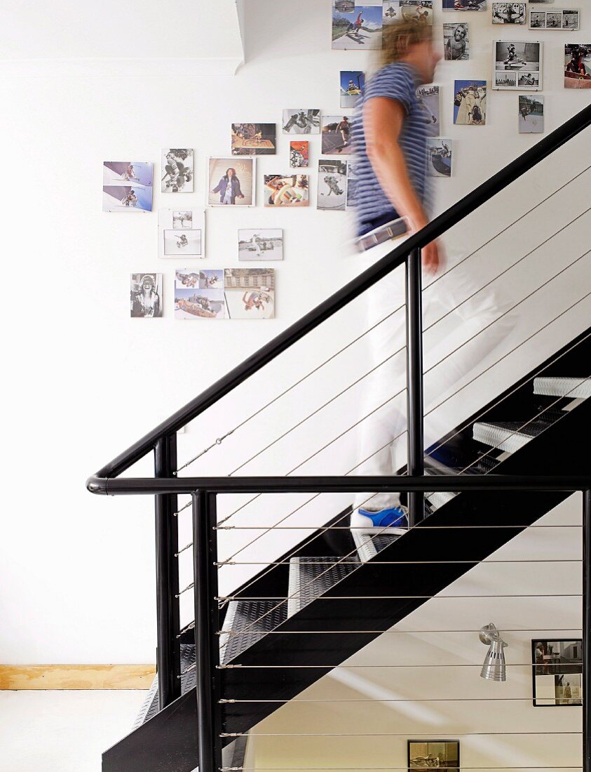Angepinnte Fotos über dem Aufgang einer schwarz lackierten Stahltreppe; Mann beim Hinaufgehen