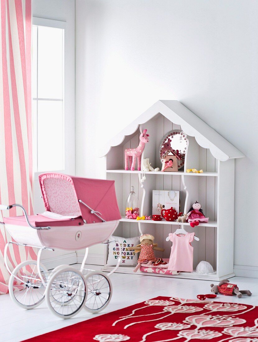 Mit Spielzeug dekoriertes, romantisches Puppenhaus und rosaroter Retro-Puppenwagen
