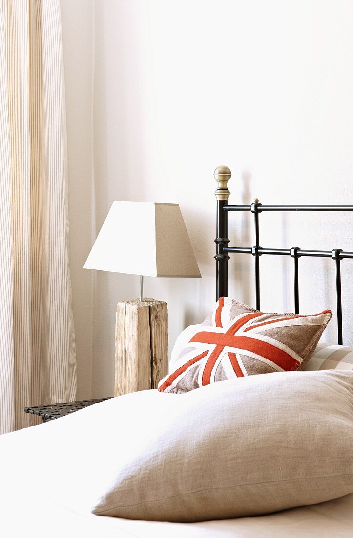 Stylised Union Flag cushion on metal bed and bedside lamp with rustic wooden base