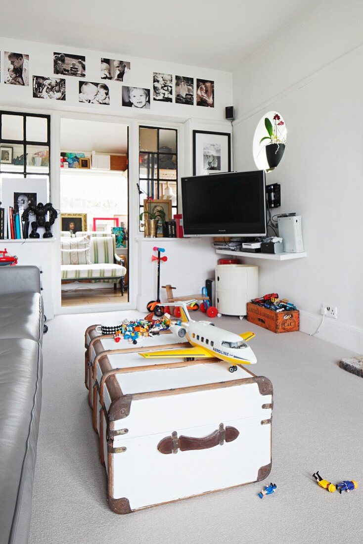 White-painted, vintage trunk and toys on pale grey carpet in living room with open door and view of traditional bench