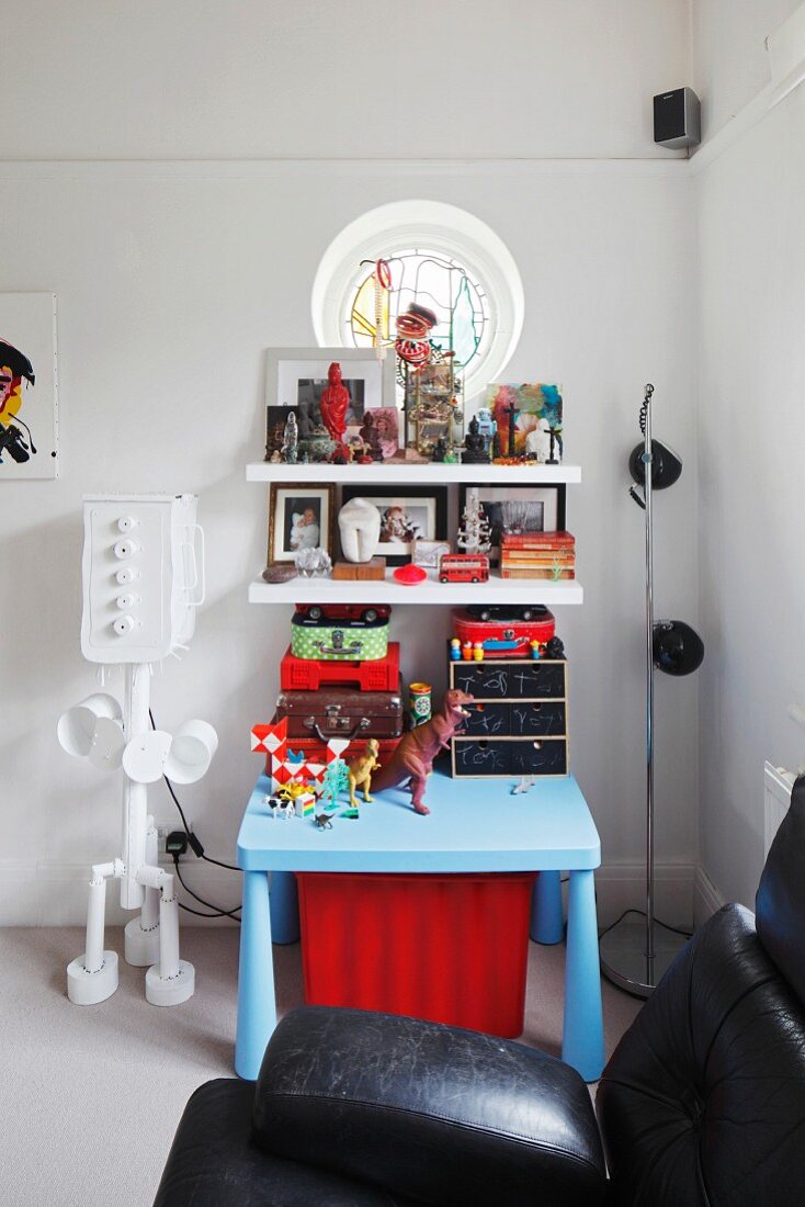Child's table painted pale blue below shelves of toys next to robot standard lamp