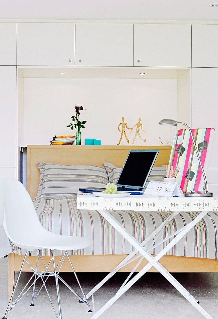 Weisser Klapptisch als mobiler Schreibtisch mit Laptop und Schreibtischlampe in modernem Schlafzimmer; beim Tisch ein Eames-Stuhl