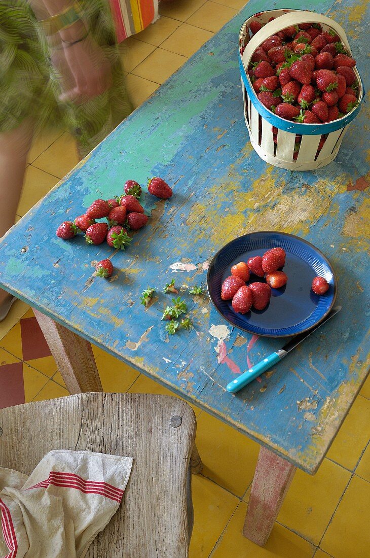 Erdbeeren auf blauem Teller und im Korb auf Vintage Holztisch