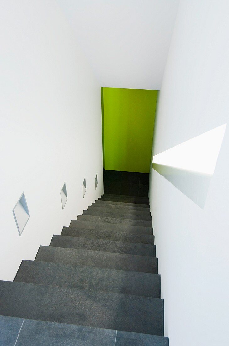Steiler Treppenabgang in weißem Treppenhaus mit eingebauten Wandleuchten