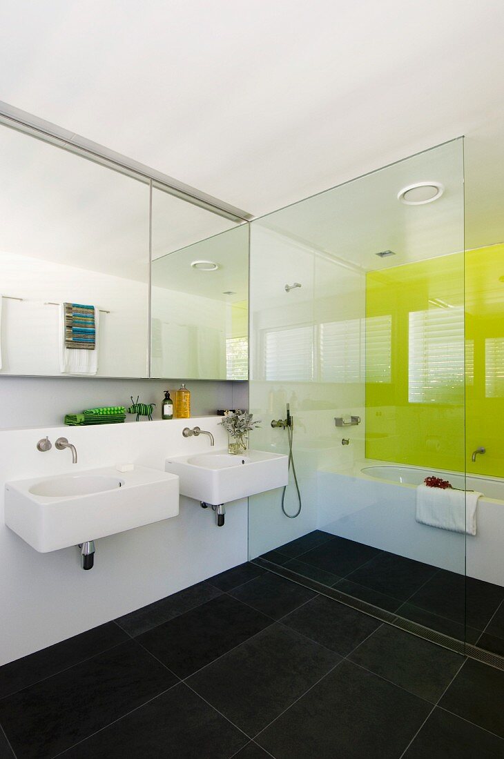 Modern, white bathroom with anthracite tiled floor and lemon yellow wall behind bathtub