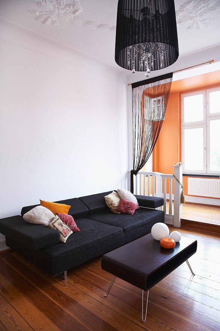 Retro coffee table with black leather cover and modern sofa on wooden floor in front of apricot window bay with platform