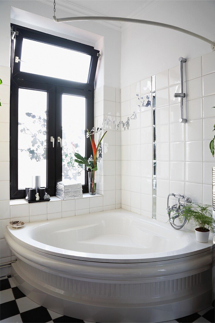 Traditional corner bathtub against tiled wall below window with dark frame