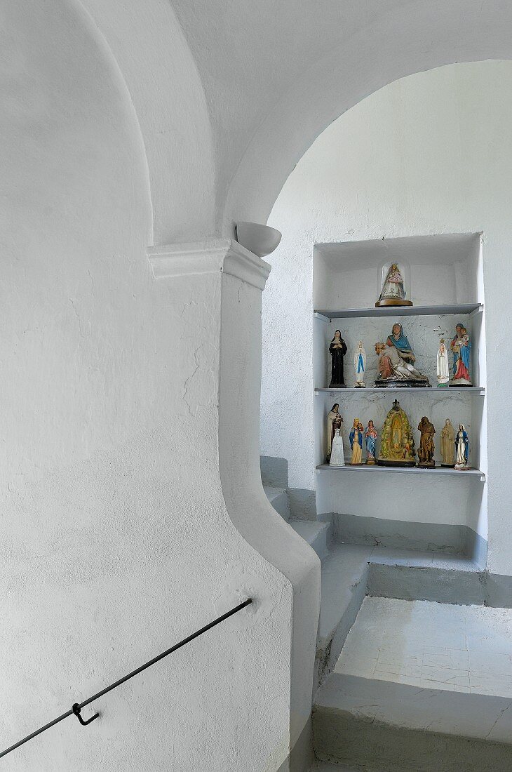 Wandnische mit sakralen Figuren in weißem Treppenhaus mit grauen Treppenstufen