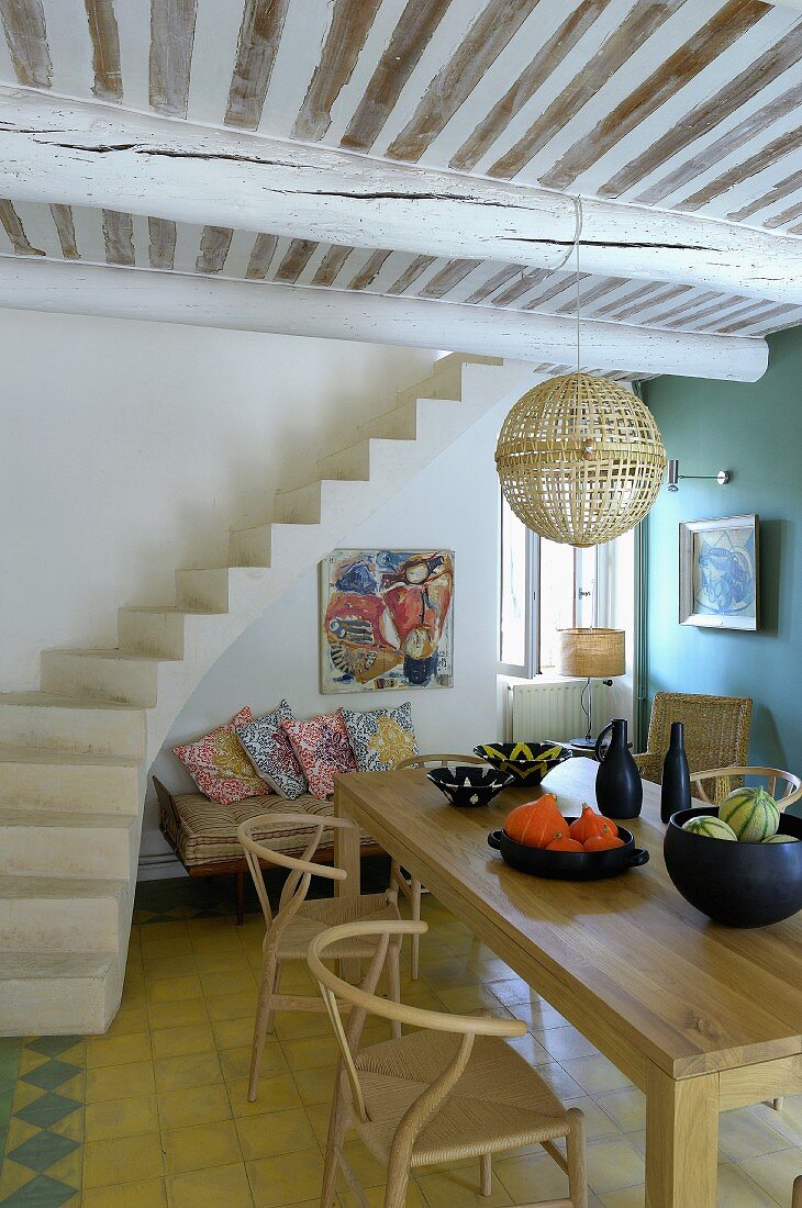 Klassiker Holzstühle am Esstisch neben betoniertem Treppenaufgang in offenem Wohnraum mit Holzbalkendecke