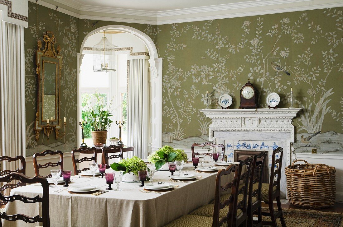 Festlich gedeckter Tisch und Kaminuhr vor floraler Tapete im Esszimmer eines englischen Landhauses