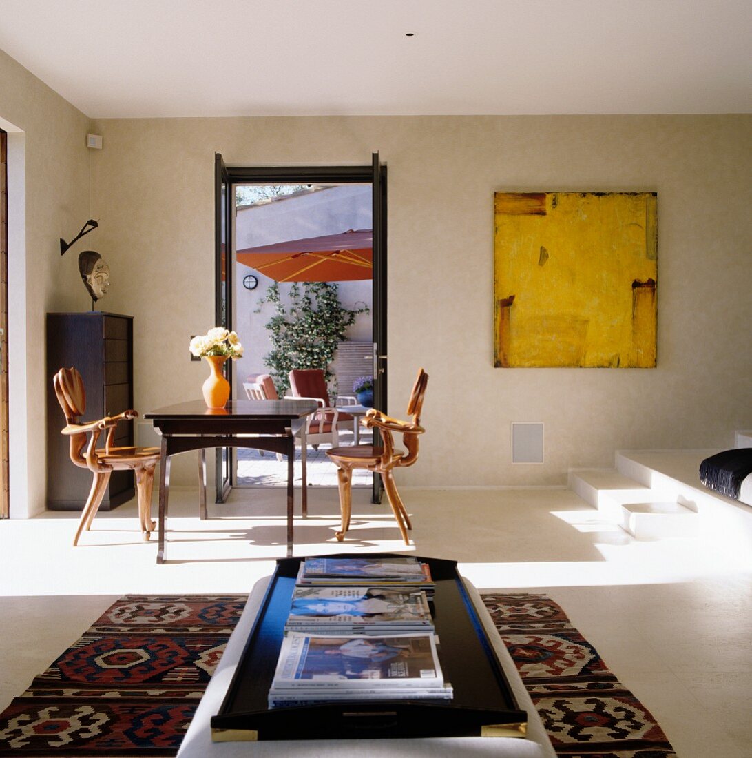 Sonniger Essplatz mit Designer-Stühlen und Blick durch offene Tür auf Terrasse; Polstertisch auf Kelimteppich
