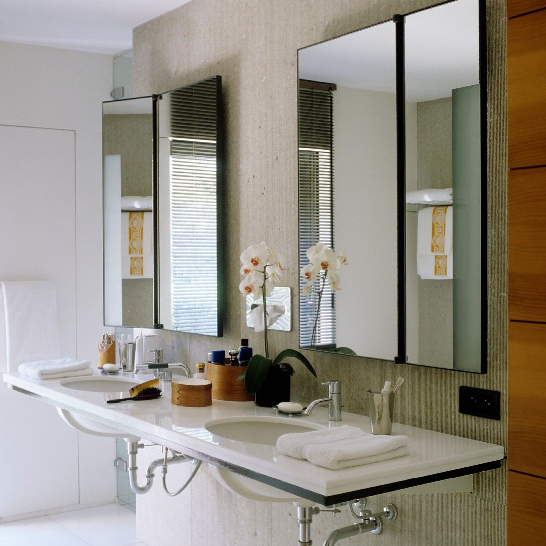 Grosser Doppelwaschtisch mit Corianplatte und asymmetrisch kippbaren Spiegeln an einer Betonscheibe