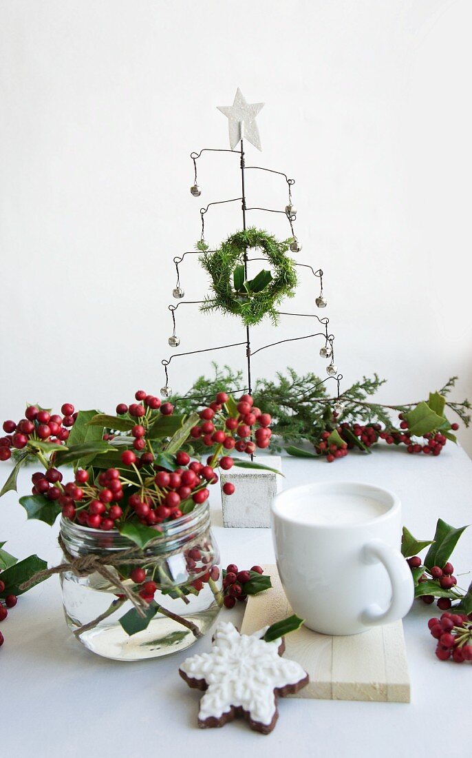 Posy of holly berries, wire Christmas tree and place setting with biscuit on table
