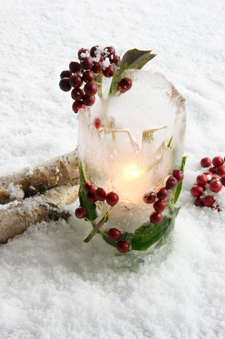Ice lantern with holly berries in snow