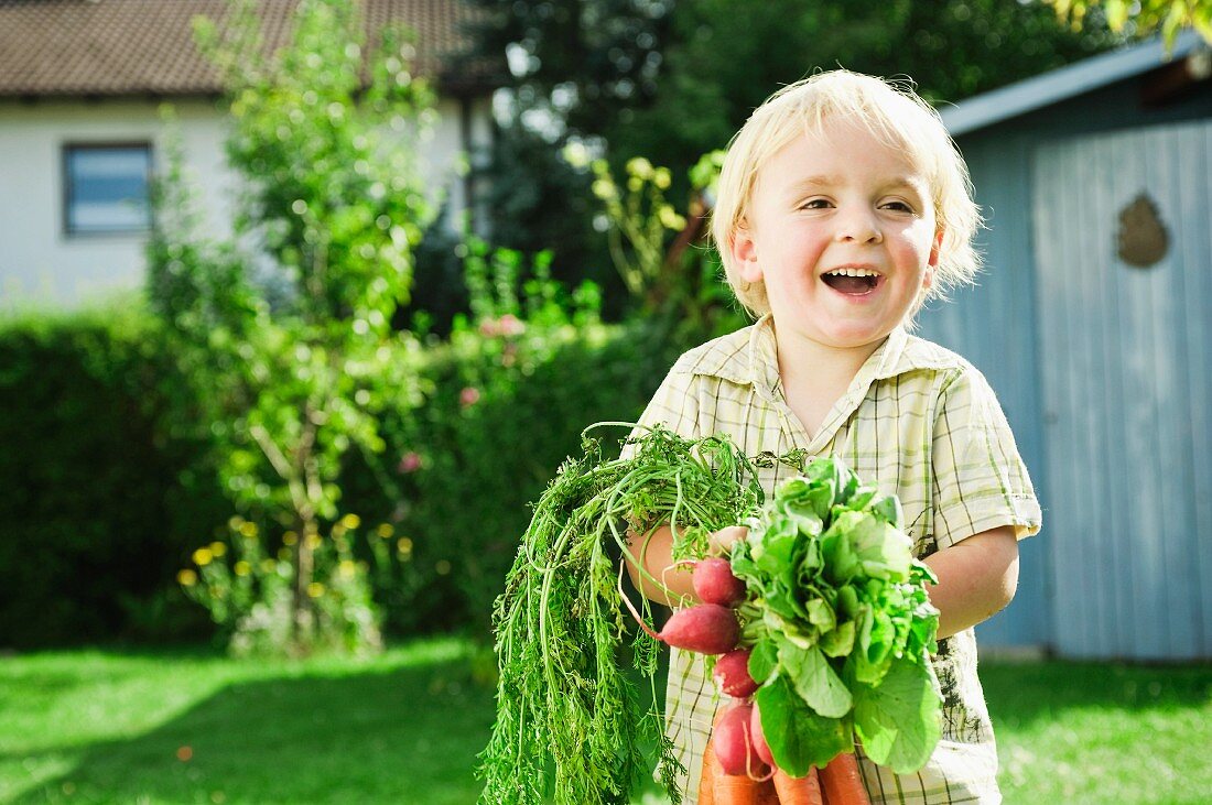 Germany, Bavaria, Boy holding radish and carrots, smiling