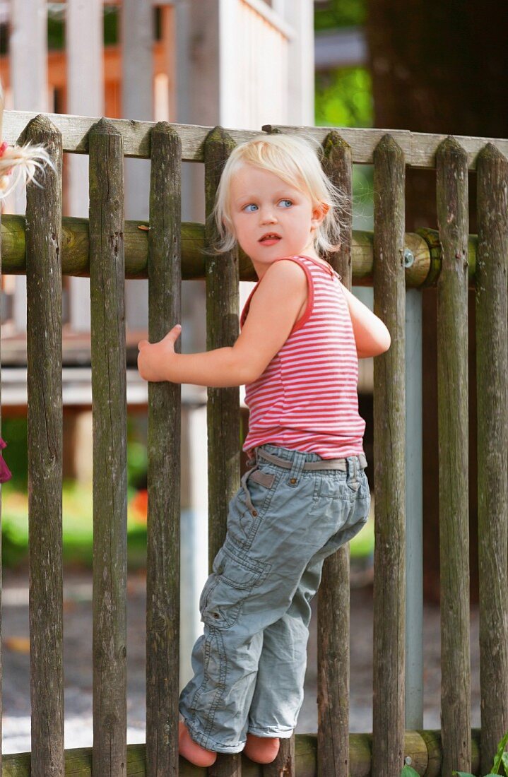 Germany, Girl standing on fence in playground