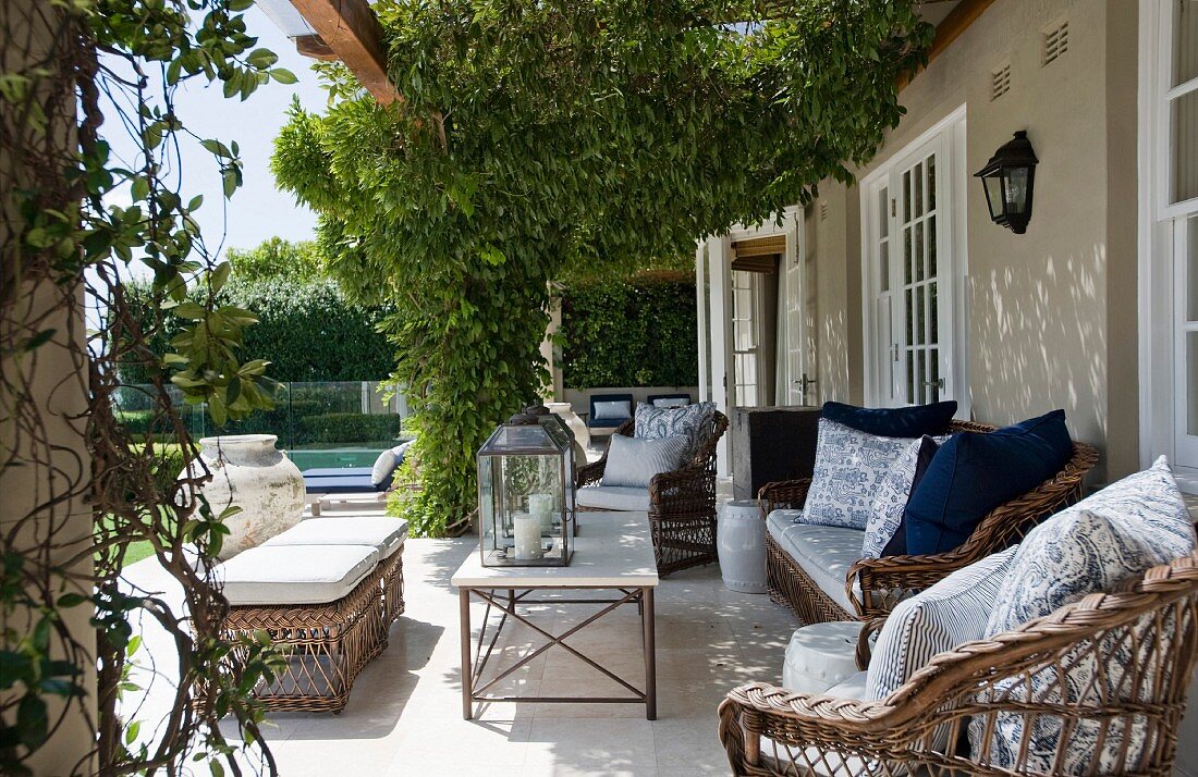 Large terrace with climber-covered pergola above rattan furniture outside traditional country house