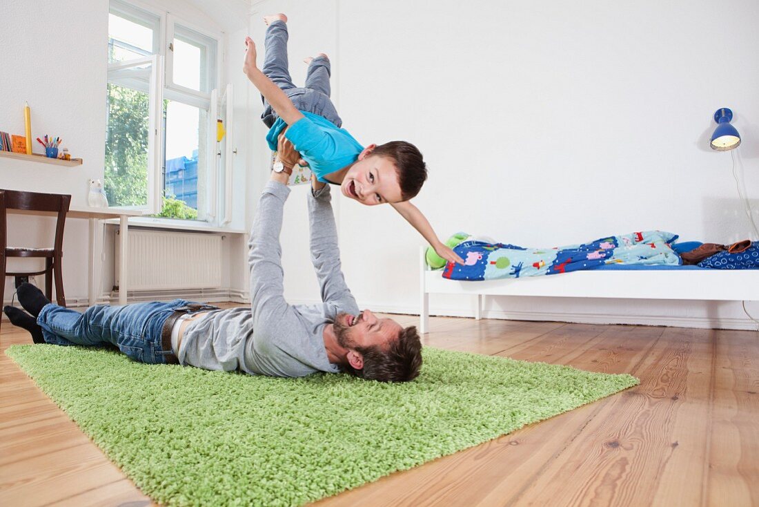 Vater liegt auf dem Teppich und hält seinen Sohn hoch