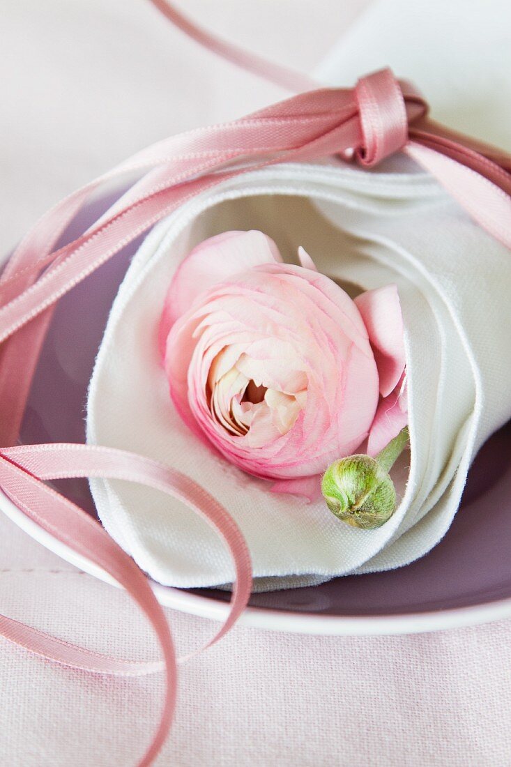 Pink ranunculus wrapped in linen napkin tied with pink ribbon