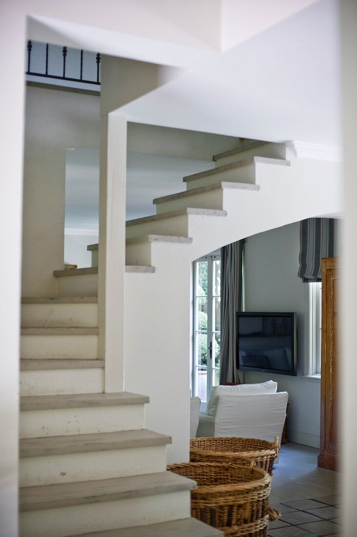 View through foyer past winding staircase in open-plan stairwell to white armchair in doorway