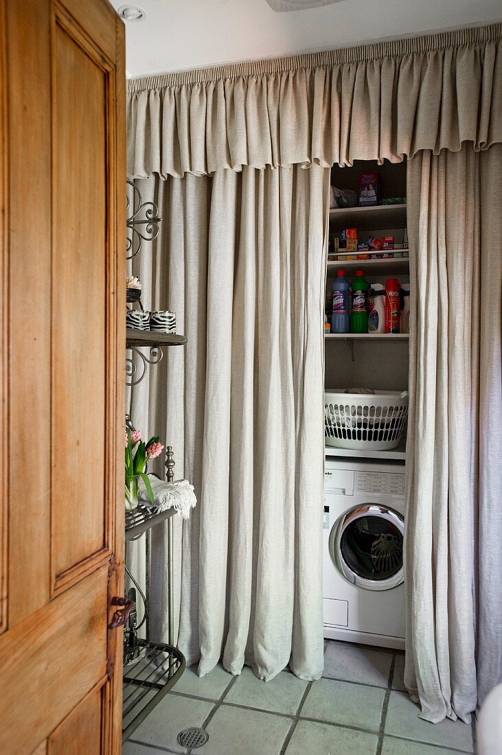 View through open door of washing machine and shelving behind floor-length curtains