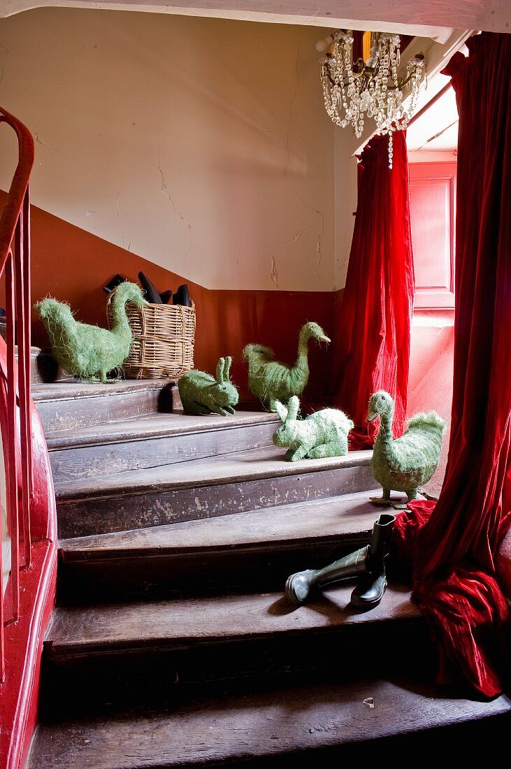 Alte Holztreppe mit Tierfiguren aus Stroh auf Stufen und roter Vorhang am Fenster