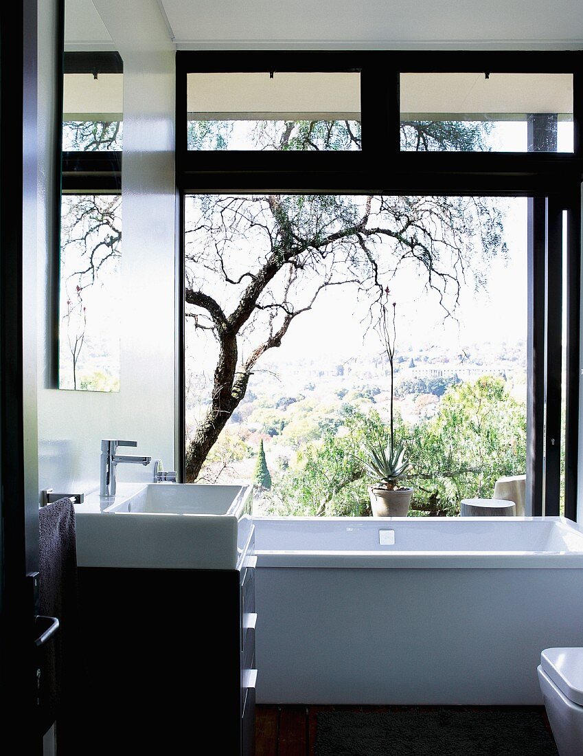Contemporary black and white bathroom with view of landscape through open sliding glass wall