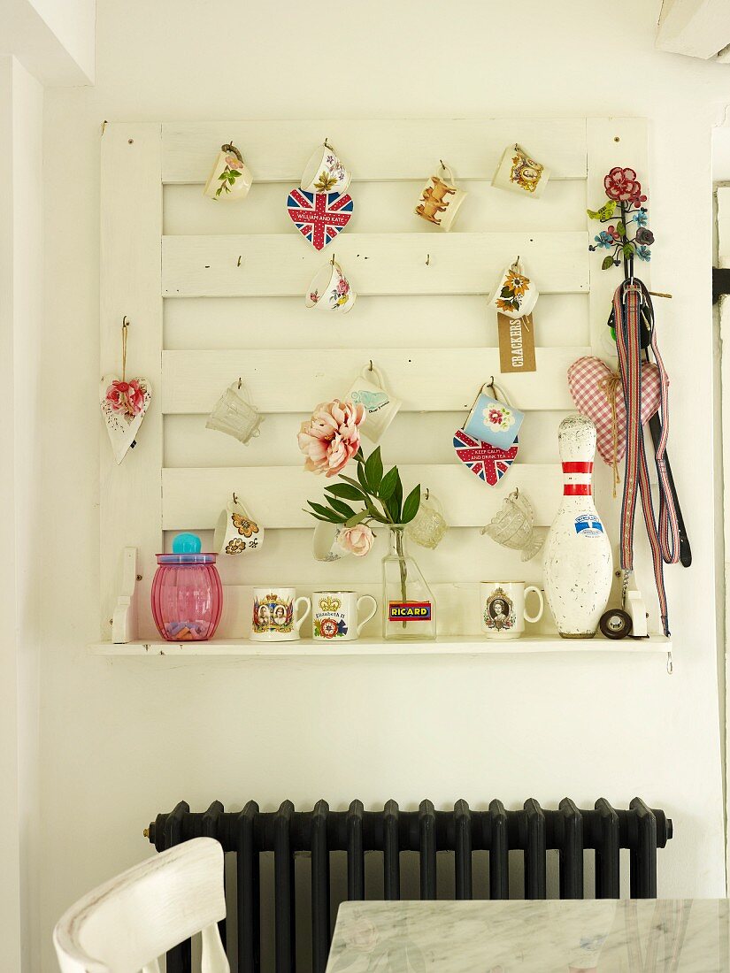 Wall-mounted peg board hung with various decorative objects above radiator in kitchen